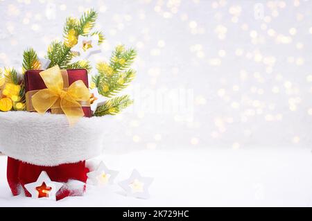 Rami in abete, scatola regalo con bulbi ad arco e a stella con luci sfocate in borsa sulla neve. Natale, Capodanno. Spazio di copia Foto Stock