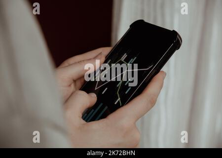 Mani femminili che tengono il telefono, controllando il grafico del mercato azionario per il tranding e l'investimento nel cambio di sicurezza. Donna in attesa di telefono Visualizza la schermata dell'indice delle azioni. Concetto di investimento di mercato azionario contabilità Finanza Foto Stock