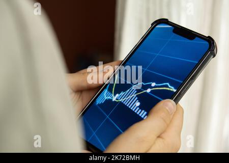 Mani femminili che tengono il telefono, controllando il grafico del mercato azionario per il tranding e l'investimento nel cambio di sicurezza. Donna in attesa di telefono Visualizza la schermata dell'indice delle azioni. Concetto di investimento di mercato azionario contabilità Finanza Foto Stock