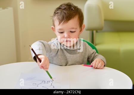 Il bambino impara a disegnare con una matita su un foglio di carta bianco. Bambino ragazzo imparando a colorare il libro. Bambino di un anno e tre mesi Foto Stock