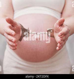 Le mani di una donna incinta in manette, nel salotto di casa Foto Stock