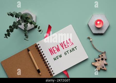 Testo nuovo anno, nuovo inizio in notebook, giornale. Fondo verde menta, giacitura piatta con rametti di eucalipto, trincetto di legno di Xmas, candela su marmo esag Foto Stock