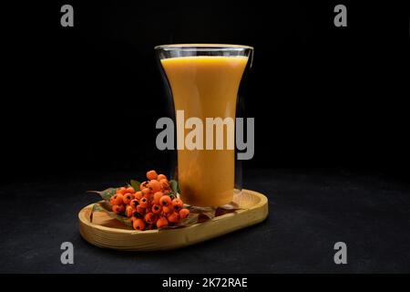 Succo di zucca appena spremuto con cenere di montagna in un bicchiere, su un asse di legno, su sfondo scuro Foto Stock