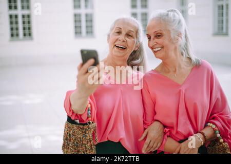 Donne anziane gemelle all'aperto in città prendendo selfie. Foto Stock
