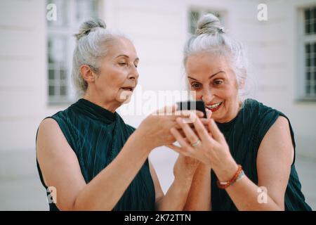 Donne anziane gemellano all'aperto in uno smartphone per il controllo della città. Foto Stock