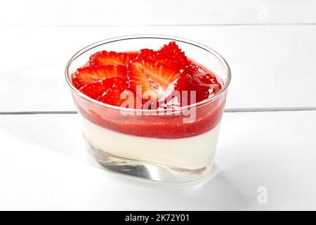 Panna cotta cremosa con coulis di fragole e rabarbaro e frutti di bosco freschi in vetro su tavolo di legno bianco Foto Stock