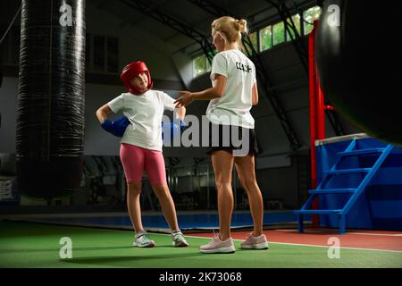 Ginnastica femminile di kickboxer con allenatore personale in palestra sportiva, al coperto. Concetto di studio, sfide, sport, hobby, competizione Foto Stock