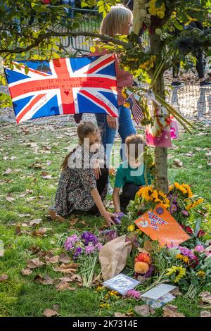 A Green Park, Londra, Regno Unito, due bambini ispezionano i tributi di fiori e altri oggetti rimasti dopo la morte della regina Elisabetta II Foto Stock