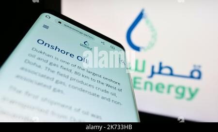 Telefono cellulare con sito web della società petrolifera Qatar Energy sullo schermo di fronte al logo aziendale. Messa a fuoco in alto a sinistra del display del telefono. Foto Stock