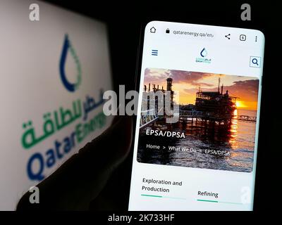 Persona in possesso di smartphone con pagina web della società petrolifera Qatari QatarEnergy sullo schermo davanti al logo. Messa a fuoco al centro del display del telefono. Foto Stock