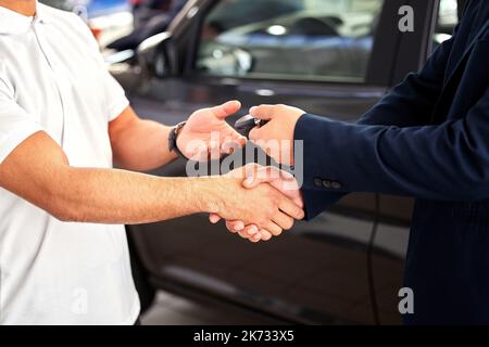 Congratulazioni per la nuova corsa. un venditore di auto che consegna le chiavi e agita la mano dei suoi clienti. Foto Stock