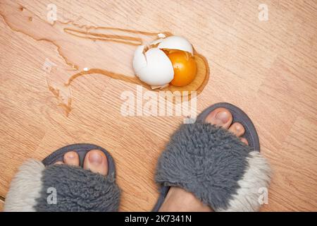 uovo rotto e piedi sul pavimento in cucina Foto Stock