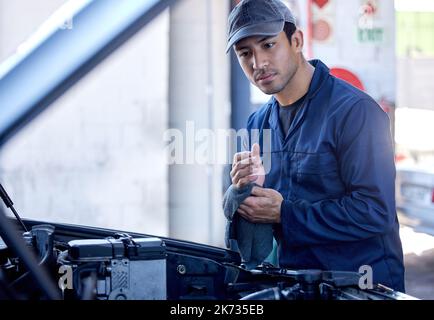 Tutto fatto. un bel giovane meccanico maschile che lavora sul motore di un'auto durante un intervento di assistenza. Foto Stock