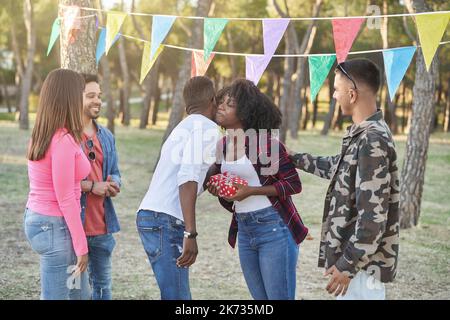 Gruppo di amici che regalano un regalo di compleanno all'amico mentre festeggia il suo compleanno all'aperto in un parco. Concetto di amicizia. Foto Stock