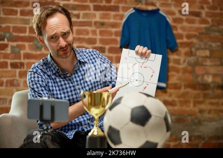 Emotivo uomo, tifoso di calcio registrazione vlog circa l'ultima partita di calcio e condivide la sua opinione sulla strategia del gioco. Sport, hobby e tempo libero Foto Stock