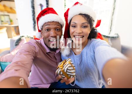 Felice coppia afro-americana che indossa la casa di babbo natale, videochiama Foto Stock