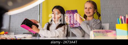 pre blogger dimostrando diverse cartoleria vicino a lampada circolare su sfocato in primo piano, banner Foto Stock