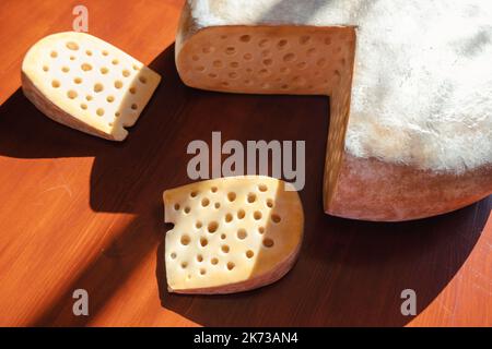 Vista ravvicinata di una ruota e del formaggio Gruyere affettato sul dorso di legno. Concetto gourmet naturale. Foto di alta qualità Foto Stock