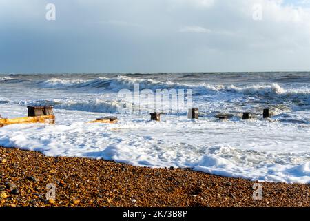 Onde che si infrangono sulla spiaggia di Bexhill-on-Sea con nuvole tempesta e una spiaggia groyne Foto Stock