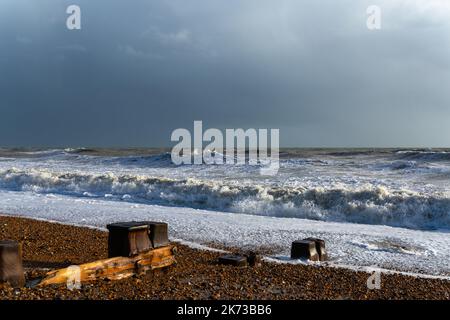 Onde che si infrangono sulla spiaggia di Bexhill-on-Sea con nuvole tempesta e una spiaggia groyne Foto Stock