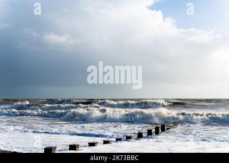 Onde che si infrangono sulla spiaggia di Bexhill-on-Sea con nuvole tempesta e una spiaggia groyne Foto Stock