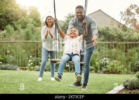 La famiglia è la cosa più importante al mondo. genitori che giocano con loro figlio sull'altalena fuori. Foto Stock