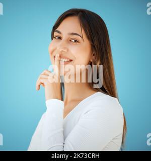 La bellezza deve essere solo un sussurro. Studio di una giovane donna che tiene il dito sulle labbra su uno sfondo blu. Foto Stock