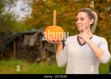 Bella donna di mezza età che tiene una piccola zucca in mano e puntando il dito in aria come un insegnante tutti prestano attenzione contro un autu Foto Stock