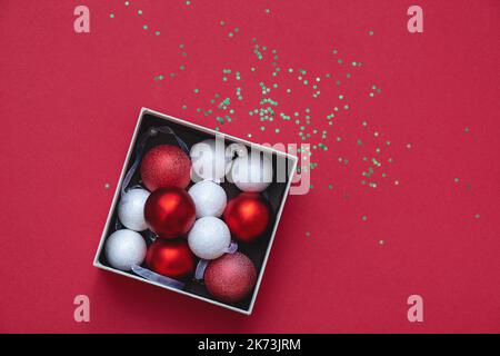 Vista dall'alto delle decorazioni rotonde di Natale in scatola regalo aperta su sfondo rosso. Bei giocattoli tondi rossi e bianchi. Concetto di Natale e Capodanno. Spazio di copia. Messa a fuoco selettiva morbida Foto Stock
