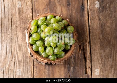 Frutti di bosco verdi in una ciotola di legno. Raccogliere bacche su un tavolo di legno. Cibo vitaminico estivo di uva spina. Foto Stock