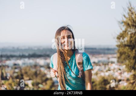 Giovane donna sorridente con uno zaino sulla cima di una collina. Fiducia in se stessi. Foto Stock