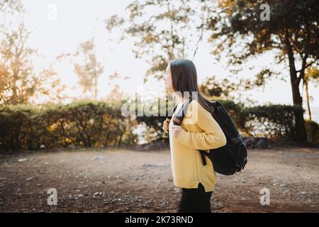 Vista laterale studente universitario che indossa un maglione giallo e uno zaino nella strada del parco del campus. Sorriso innocente Foto Stock