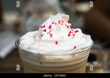 Vetro di plastica Frapuccino con panna montata e gocce di cioccolato colorate sulla parte superiore. Bevanda dolce fresca e congelata Foto Stock