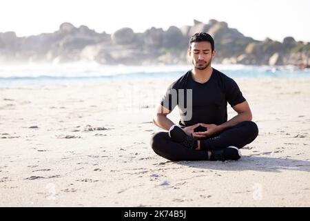 Trovare zen. Scatto completo di un bel giovane atleta maschile meditato sulla spiaggia. Foto Stock