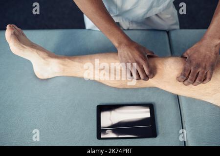 Vista ad angolo alto del terapista che effettua un massaggio medico al paziente sul lettino utilizzando un tablet digitale Foto Stock
