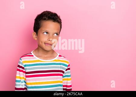 Foto di carino pensieroso ragazzo positivo con capelli ricci vestito a righe lungo manica guardare spazio vuoto isolato su sfondo di colore rosa Foto Stock