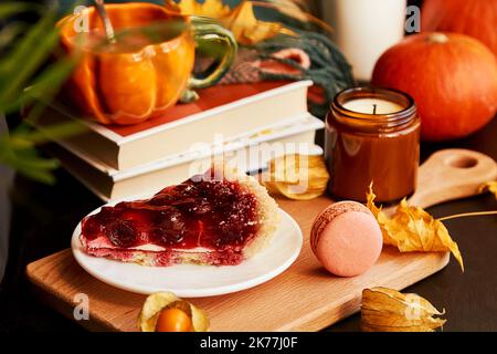 Tazza di caffè a forma di zucca, torta di ciliegie, amaretti, zucca, candela tra decorazioni autunnali. Primo piano sfocato. Casa accogliente Hygge. Foto Stock