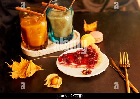 Bicchieri di latte di zucca, bastoncini di cannella e torta di ciliegie. Caffè stagionale in autunno. Accogliente higge casa estetica. Foto Stock