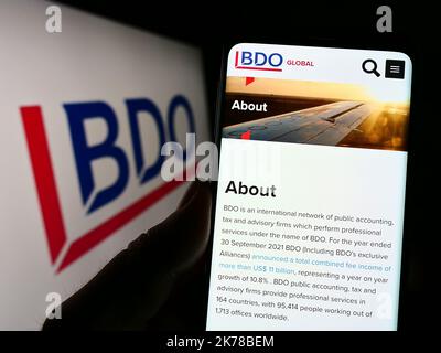 Persona che tiene il cellulare con pagina web della rete di contabilità BDO Global sullo schermo di fronte al logo aziendale. Messa a fuoco al centro del display del telefono. Foto Stock