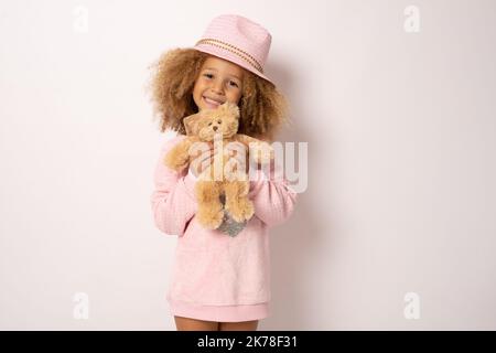 bellissimo bambino afroamericano che indossa un cappello di paglia che abbraccia un orsetto di peluche e sorride alla macchina fotografica isolata su bianco Foto Stock