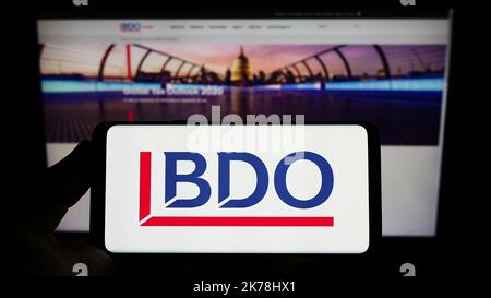 Persona che tiene uno smartphone con il logo della rete contabile BDO Global sullo schermo davanti al sito Web. Messa a fuoco sul display del telefono. Foto Stock