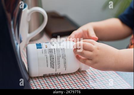 Un bambino sta cercando di raggiungere e aprire un biberon a prova di bambino con vitamine o integratori Foto Stock