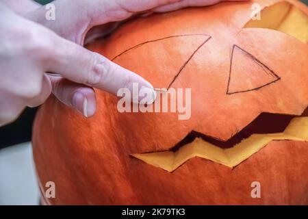 Donna che usa un coltello di zucca intagliata o Jack-o'-latern a casa. Un primo piano di mani e zucca. Halloween, decorazione e concetto di festa Foto Stock