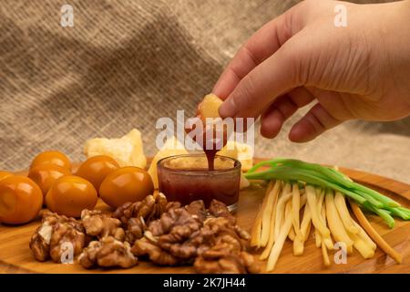 Qualcuno immerge un pezzo di formaggio nel miele sullo sfondo di diverse varietà assortite di formaggio Foto Stock