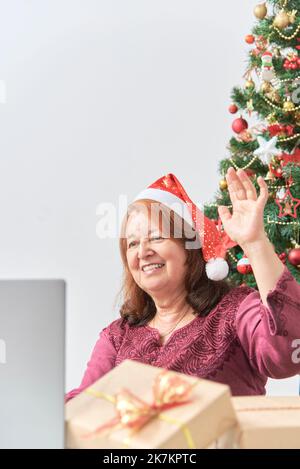 Donna ispanica matura che saluta i suoi cari tramite videochiamata durante Natale con il suo laptop. Concetti: La gioia di condividere durante le vacanze, il Foto Stock