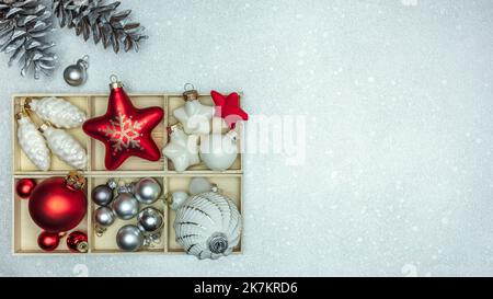 scatola con colorati ornamenti dell'albero di natale. festoso sfondo argentato con coni di pino. Foto Stock