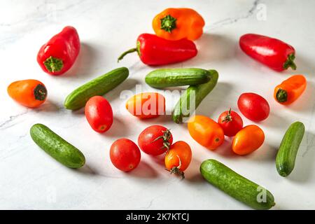 Mini verdure su marmo bianco pronte per cucinare e mangiare. Pomodori ciliegini, mini cetrioli e mini peperoni Foto Stock