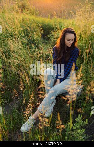 Ritratto di una bella giovane donna sul prato guardando il tramonto godendo la natura estate sera all'aperto. Foto Stock