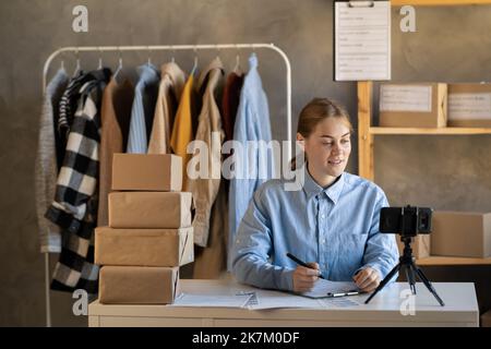 Giovane donna imprenditore in negozio di abbigliamento online utilizzare smartphone live streaming per la vendita di abbigliamento moda al cliente e presentare dettagli sul sociale Foto Stock