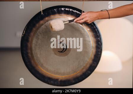 Primo piano della mano di una donna che batte un gong con un martello. Gong e frusta per gong Foto Stock